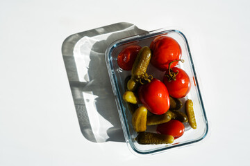 Pickled tomatoes with tails and cucumbers in a glass container on a white background with a nice shadow