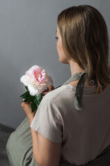 A girl with a peony in her hands in a linen apron, half-turned.
