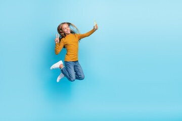 Fototapeta na wymiar Full length portrait of energetic active girl jumping make selfie show v-sign isolated on blue color background