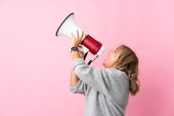 Middle aged blonde woman over isolated pink background shouting through a megaphone to announce...