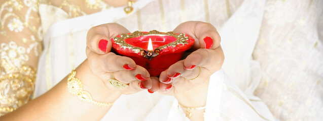 Woman holds red diya lamp or light with both hands on the occasion of Diwali and it has flame of fire.