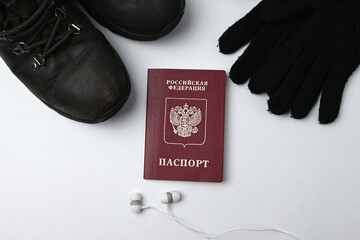Russian passport with shoes, gloves and ear buds on a white background. Young men from Russia walking for hours to flee mobilization with light luggage