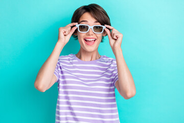 Portrait of positive cheerful woman with bob hairstyle wear striped t-shirt hands touch 3d glasses isolated on turquoise color background