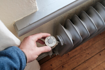 Hand turns the thermostat to minimum on the radiator. Concept of crisis and energy saving, due to...