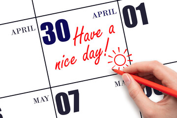 The hand writing the text Have a nice day and drawing the sun on the calendar date April 30