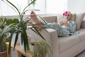 Young pink haired woman relaxing on sofa and reding ebook or social media or serfing internet