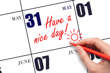 The hand writing the text Have a nice day and drawing the sun on the calendar date May 31