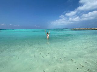 Fototapeta na wymiar Slim girl in a white swimsuit in an empty turquoise ocean with her arms up in the air. Wide Lens Photo