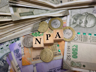 NPA or non performing asset by letters on wooden beads or block with Indian rupee notes and coins.