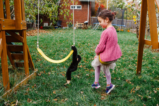 A little girl swings happily next to toy stuffed monkey in yard