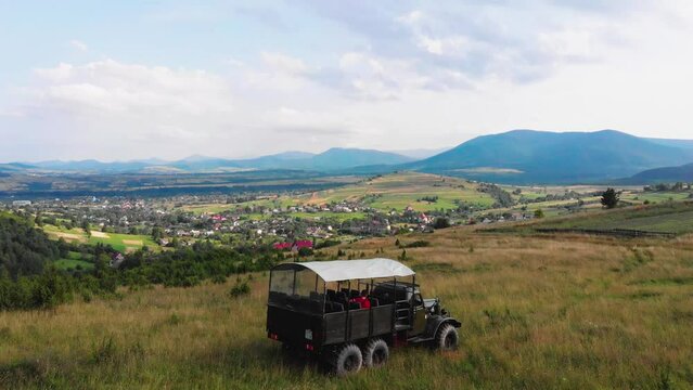 The truck is traveling along a mountain road on tourist route. A tourist trip through Ukrainian Carpathians in the summer. Big green tourist car Zil. Rest in nature among the river and green forests.