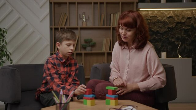 Boy with autism building with wooden blocks doing tasks of autism therapist. School boy with autism studying with teacher. Autism Spectrum Disorder education.