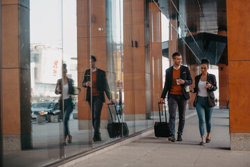 Business man and business woman talking and holding luggage traveling on a business trip, carrying fresh coffee in their hands.Business concept