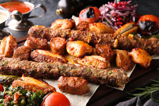 Turkish cuisine. Fried meat, chicken, kebab. Fried vegetables: tomatoes, peppers, onions, pomegranate seeds on pita bread with herbs. Red and white sauces on a black table, salad. Background image