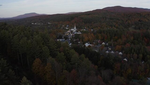 A drone flys away Stowe, Vermont as the sunsets over the little mountain village.  Autumn has taken over the area.  The leafs are starting to change colors.