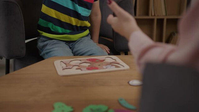 School boy solving wooden puzzle sitting at psychologist office. Awareness of children's mental health. Over the shoulder view.