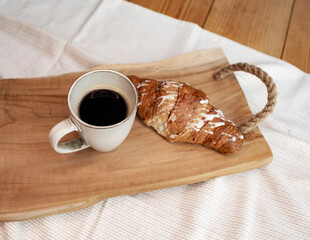 A cup of black coffee with croissant on wooden tray