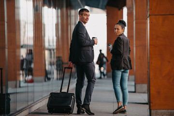 Fototapeta na wymiar Business man and business woman talking and holding luggage traveling on a business trip, carrying fresh coffee in their hands.Business concept