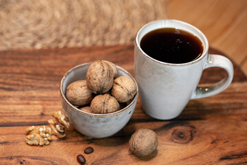 A cup of black hot coffee and a bowl full of walnuts on the wooden table