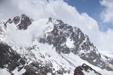 Rocky mountain slope, at the top of a peaked rock, there is snow, sky with clouds, winter in the mountains