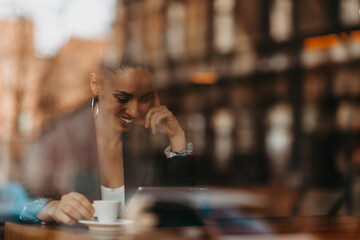 woman in a coffee shop drink coffee viewed through glass with reflections as they sit at a table chatting and laughing