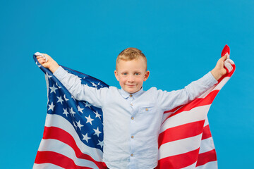 Cute boy holding American flag in indoor studio on blue background.