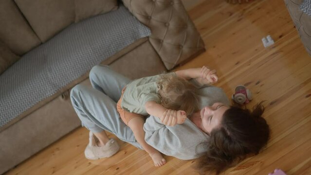Happy carefree mother and cute small child son tickling laughing having fun lying on floor and playing, smiling mum enjoying bonding cuddling hugging spending time with little funny kid at home