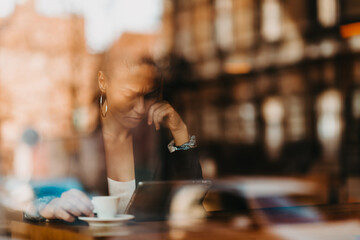 woman in a coffee shop drink coffee viewed through glass with reflections as they sit at a table chatting and laughing