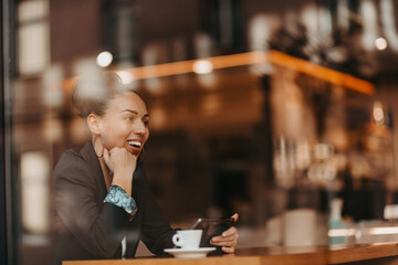 woman in a coffee shop drink coffee viewed through glass with reflections as they sit at a table chatting and laughing