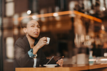 woman in a coffee shop drink coffee viewed through glass with reflections as they sit at a table chatting and laughing