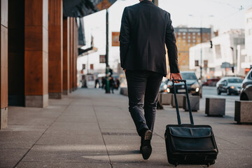 Fototapeta na wymiar Going to airport terminal. Confident businessman traveler walking on city streets and pulling his suitcase drinking coffee and speaking on smartphone