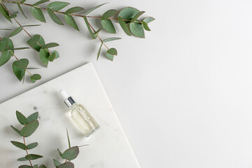 Glass bottle of serum on marble podium and green eucalyptus branches on light grey background top...