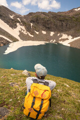 Man with Yellow Backpack Hiking to Alpine Lake with Wildflowers in Colorado Rocky Mountains