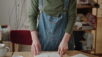 Female reading recipe book in kitchen. Tilt up view of brunette turning pages and reading recipe in notepad while standing near table in kitchen at home.