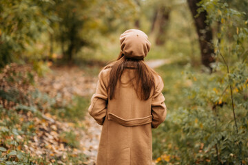 A girl in a woolen coat walks in a beautiful autumn park.