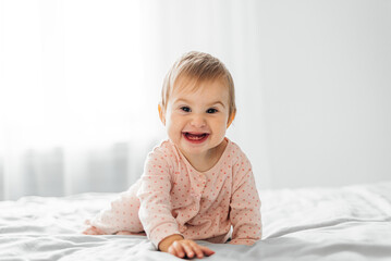 Cheerful little girl baby with two first teeth sits on the bed