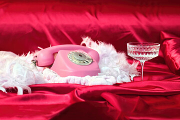 Pink old phone with feathers on red silk fabric with crystal glass. Glamor.