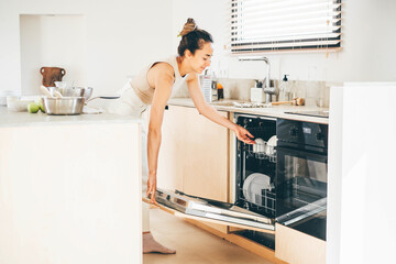 Woman washes dishes in the dishwasher at the kitchen,