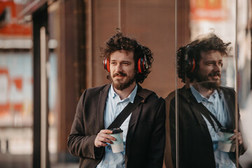 Trendy businessman with leather briefcase in financial district using smartphone while listening audio songs headphones drinking coffee