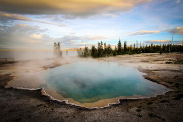 Steam coming off of a geyser in Yellowstone National Park - crystal blue water, stunning sky, near sunset.