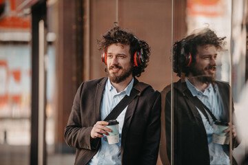 Trendy businessman with leather briefcase in financial district using smartphone while listening audio songs headphones drinking coffee