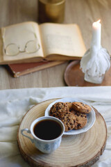 Cup of tea or coffee, plate of chocolate chip cookies, open book, reading glasses, candle and vase with flowers. Selective focus.