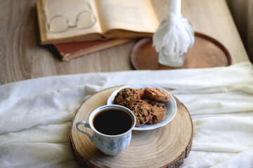 Cup of tea or coffee, plate of chocolate chip cookies, open book, reading glasses, candle and vase with flowers. Selective focus.