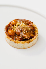 Photo of a delicious modern style handmade mini tart tartlet fulled with differ nuts like pistachio and hazelnut with salted caramel sause on a modern porcelain white flat plate on white background
