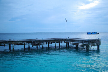 Naklejka premium View of the pier and the ocean in the evening on a resort island in the Maldives, the ship is visible on the horizon in the distance