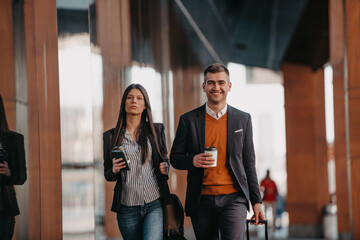 Business man and business woman talking and holding luggage traveling on a business trip, carrying fresh coffee in their hands.Business concept