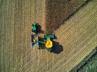 Aerial view of green tractors harvesting the crops in the large field - obrazy, fototapety, plakaty