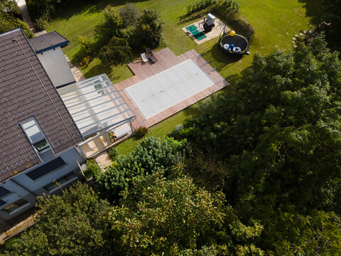 Drone photo of pool which is covered with grey pool tarpaulin, cover and prepared for winter and a garden with house