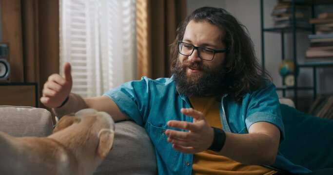 A smiling happy man plays with a cream-colored cute dog. He calls out to the pet, which comes running to snuggle with its owner. Caring for a four-legged friend.