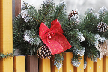 A red bow with bells hangs on a spruce garland with cones